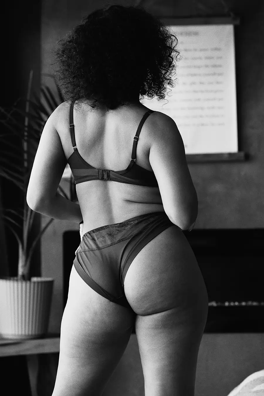Black and white photo of a woman with natural curves and stretch marks standing in lingerie."
