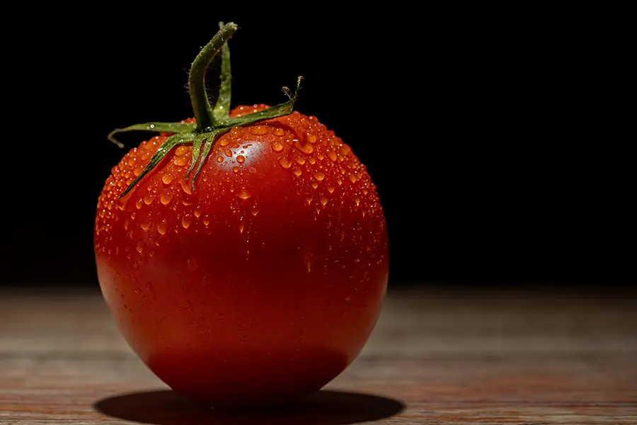 Close-up of a ripe red tomato with water droplets on a dark background.