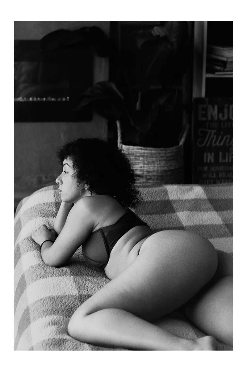 Woman lying on a bed in lingerie, photographed in black and white with natural curves and soft light.