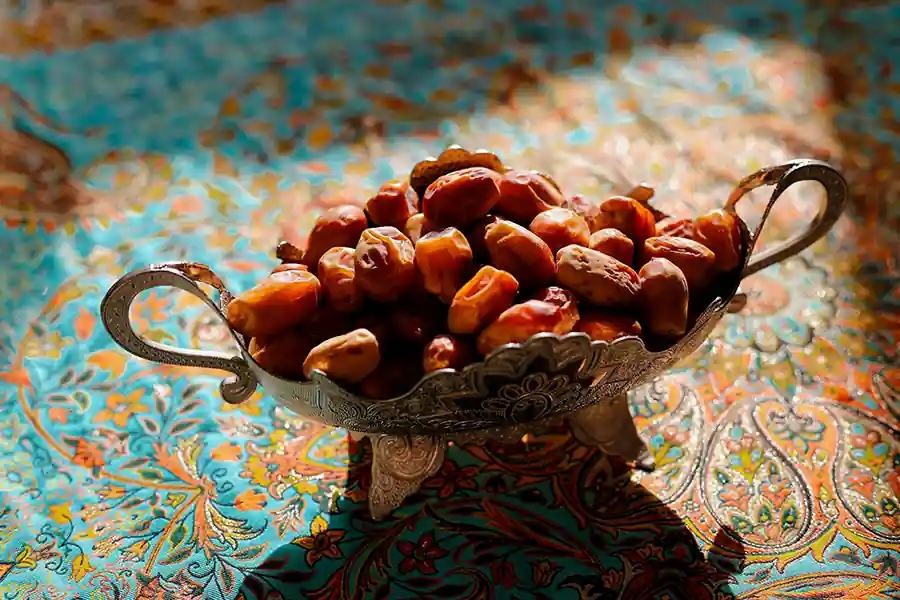 A silver bowl filled with sunlit dates on a patterned turquoise cloth creating a warm still life scene rooted in natural nourishment.