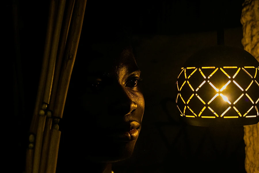 A woman’s face lit by a small lantern in the dark, her expression quiet and reflective as she looks toward the light.