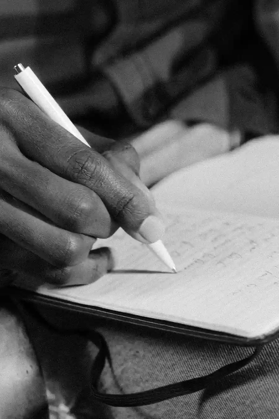 A close-up of a hand writing in a notebook with a white pen, captured in black and white to symbolize clarity, focus, and personal commitment.