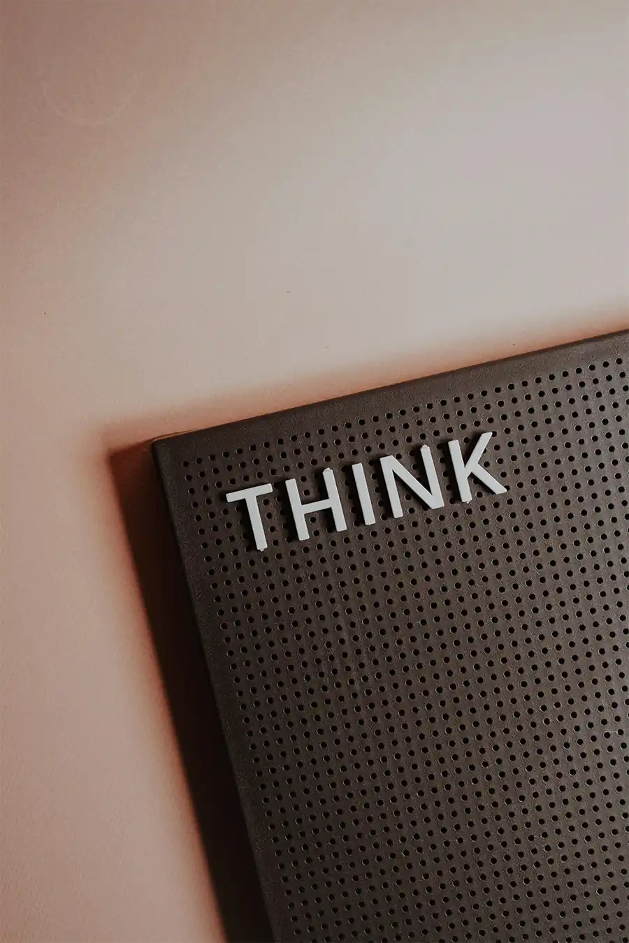 Minimalist photo of a perforated board with the word THINK in white letters on a soft beige background, symbolizing clarity, planning, and intentional goal-setting.