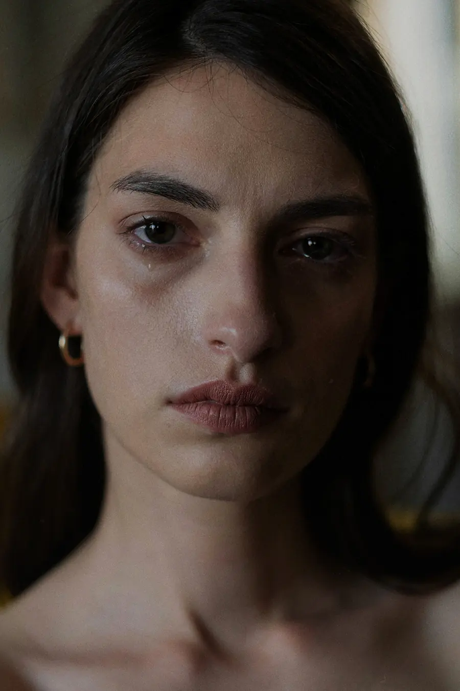 Close-up portrait of a woman with a tear on her cheek, looking straight ahead with a quiet expression, capturing the raw emotion of heartbreak.