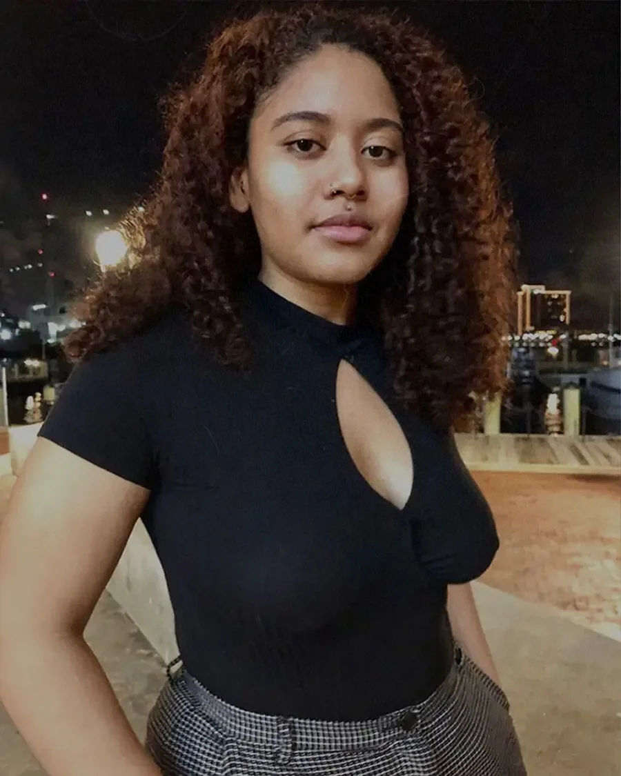 Black girl with curly hair wearing a black shirt, confidently posing and embracing her natural body.