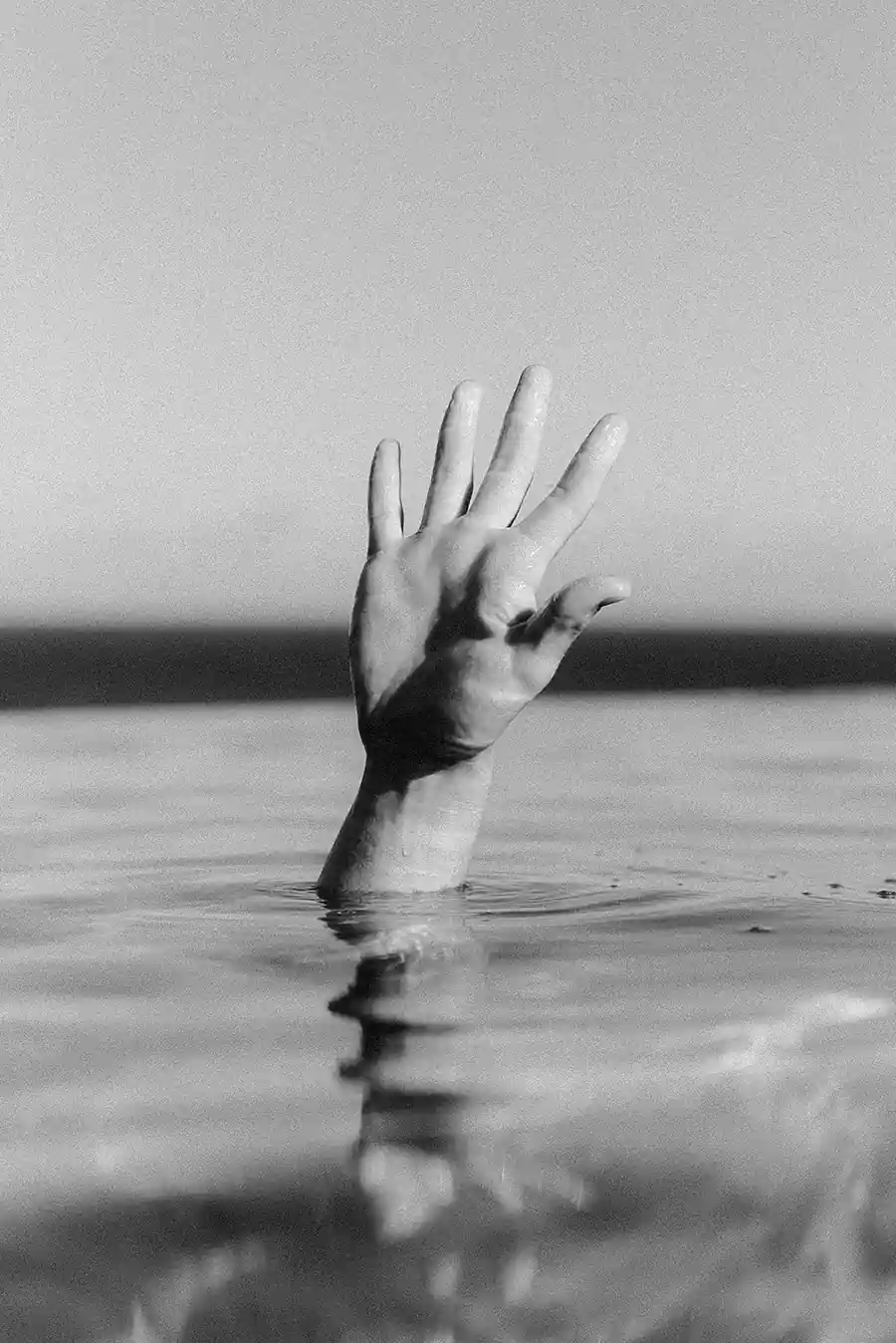 Black-and-white photo of a hand emerging from the water, symbolizing panic, overwhelm, and the feeling of being pulled under.