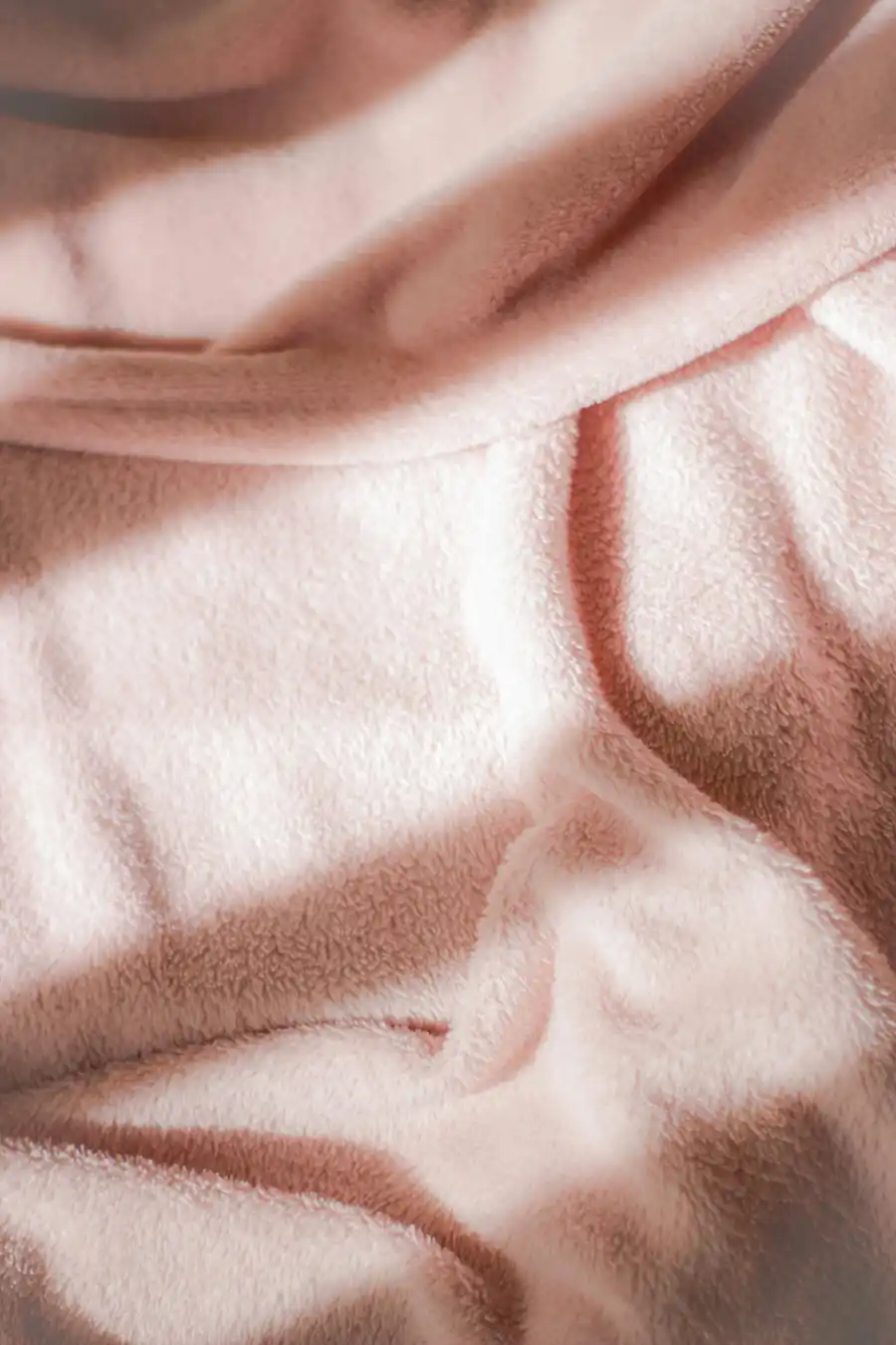 Soft pink fabric photographed in natural light with gentle shadows and textured folds creating a calm, introspective mood.