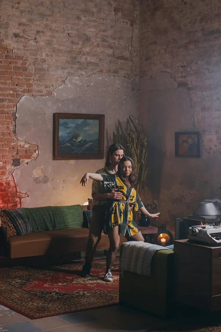 A cinematic scene of a woman dancing in a dim, vintage-style living room as a partner holds her from behind, their bodies moving slowly in warm, atmospheric light.