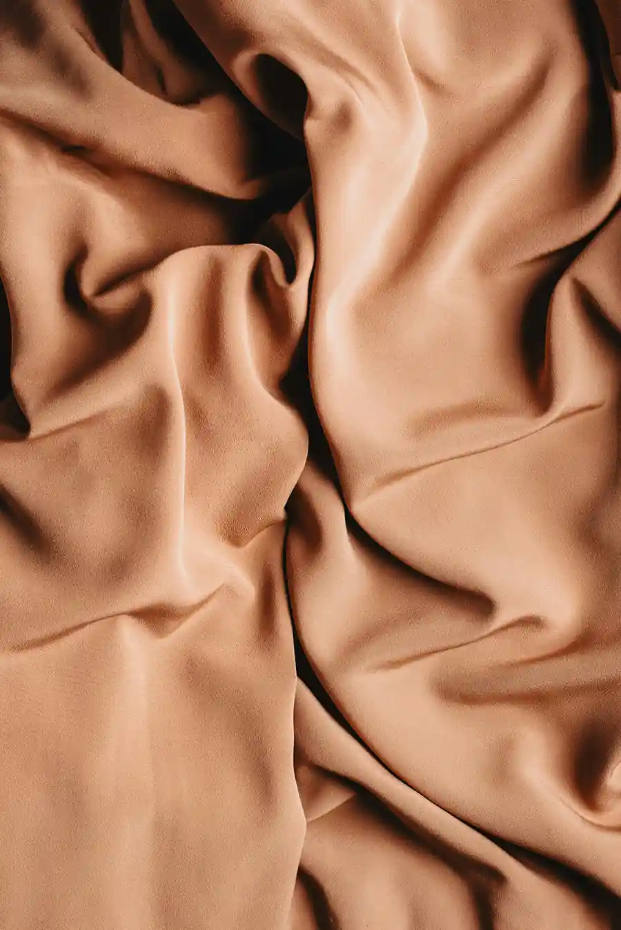 Close-up of softly folded nude-toned fabric with smooth texture and natural shadows