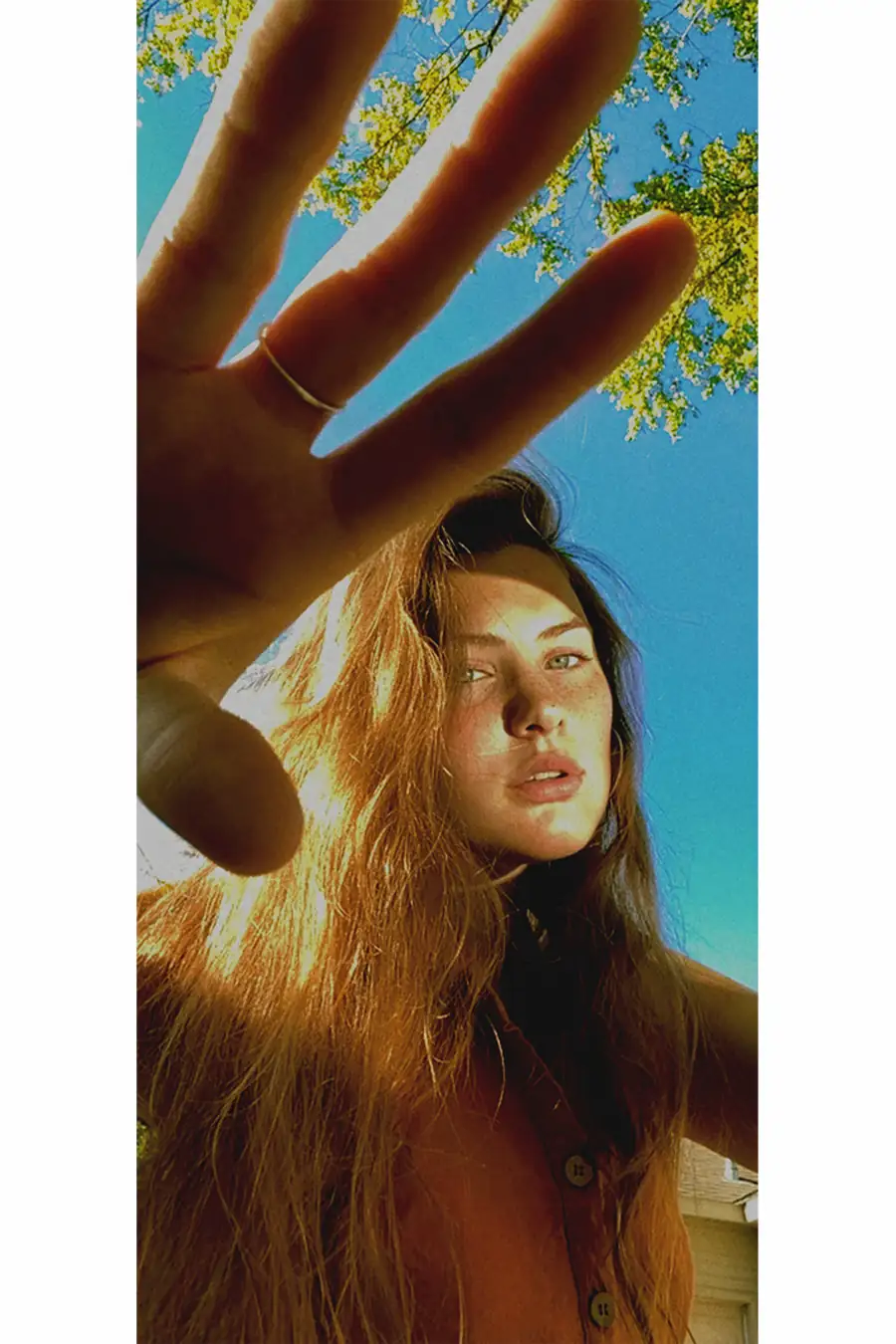 Bare Model Gibson photographed outdoors during a FaceTime photoshoot, hand reaching toward the screen in direct sunlight.
