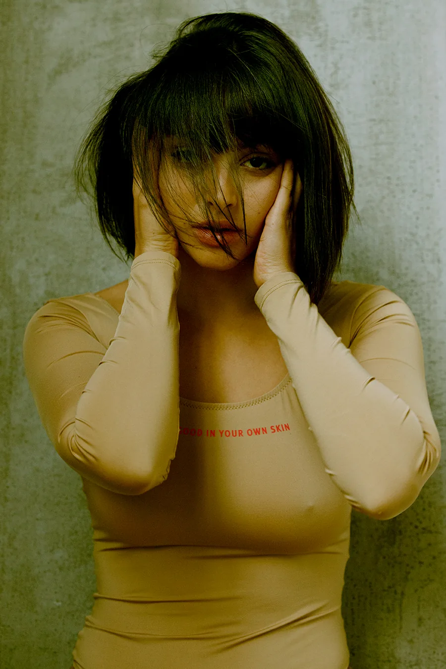 Close portrait of Irene Noren with hands framing her face, photographed in soft natural light emphasizing skin and presence