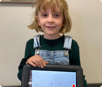 Mae, a young girl, smiling and holding up a tablet with a drawing on the screen.