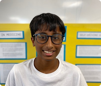 Akhil, a boy wearing glasses, smiling in front of a yellow science fair display board.