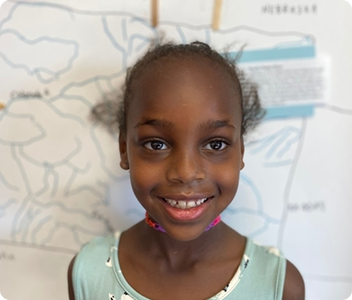 Ayana, a young girl, smiling in front of a classroom map display.