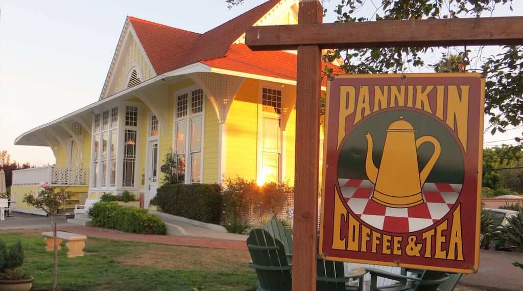 Old yellow building with white trim and pannikin sign in front.