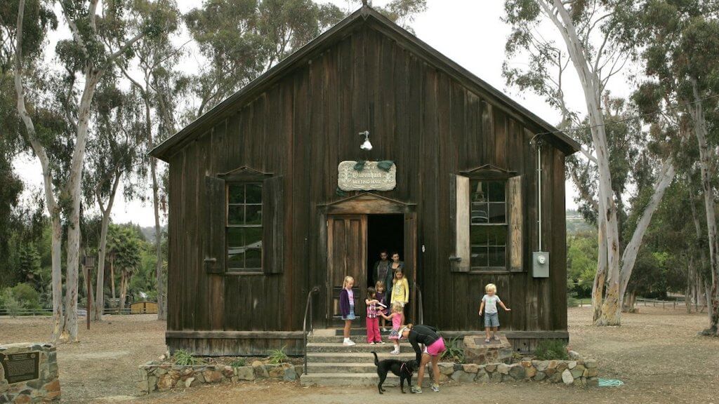 Old brown building with children and a dog standing in front.
