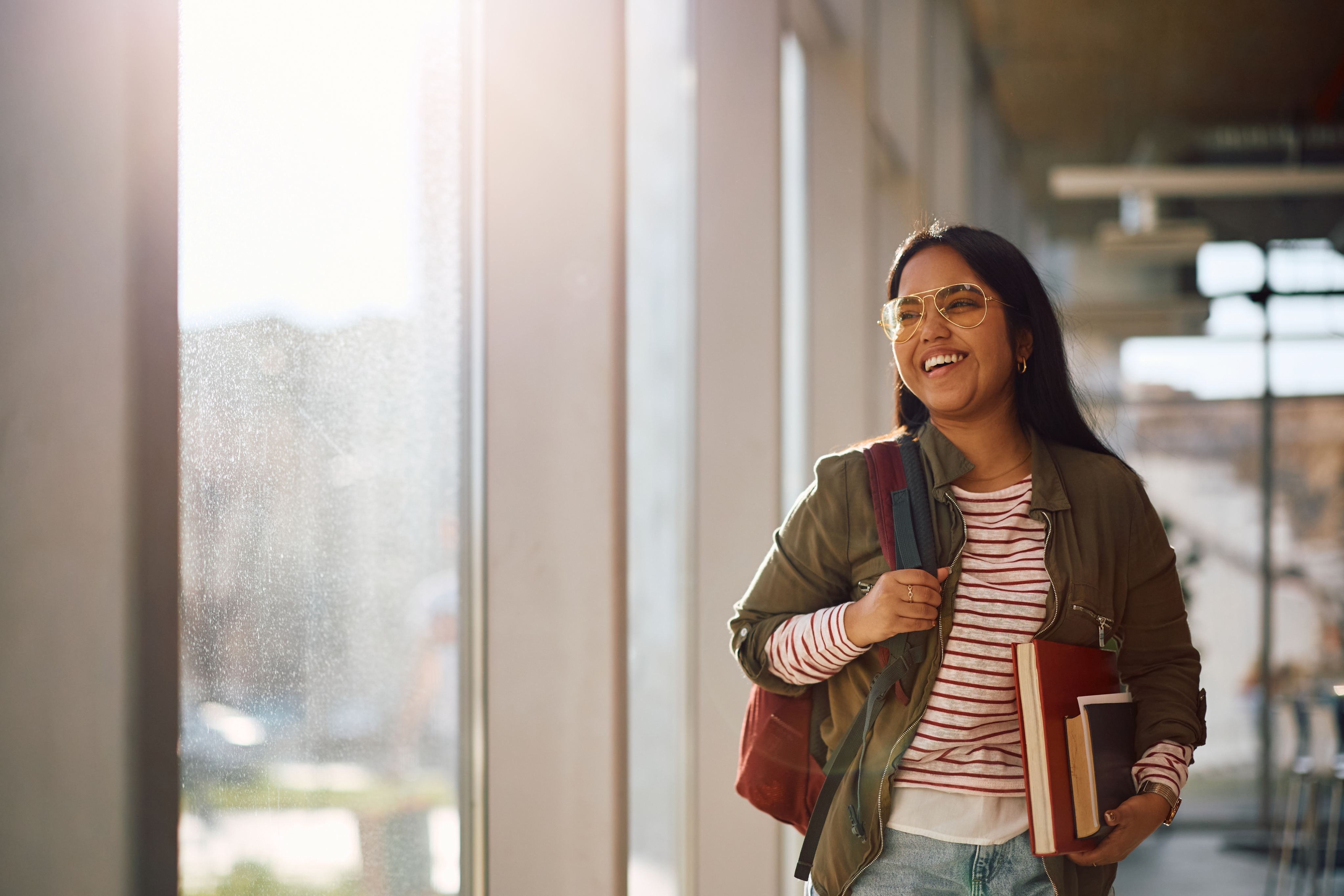 Smiling student walking through a campus hallway holding books