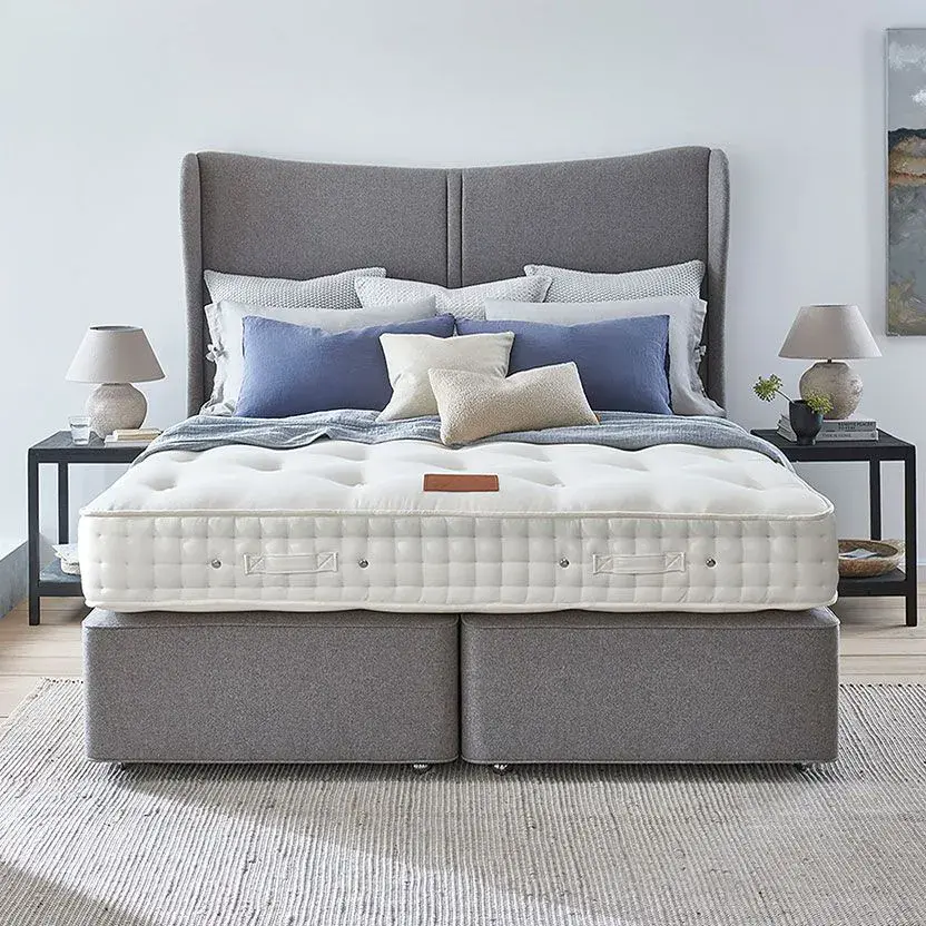 The Hypnos Organic 4 Mattress in a bedroom showroom setting with a grey bed frame and headboard and mix of pillows on the bed
