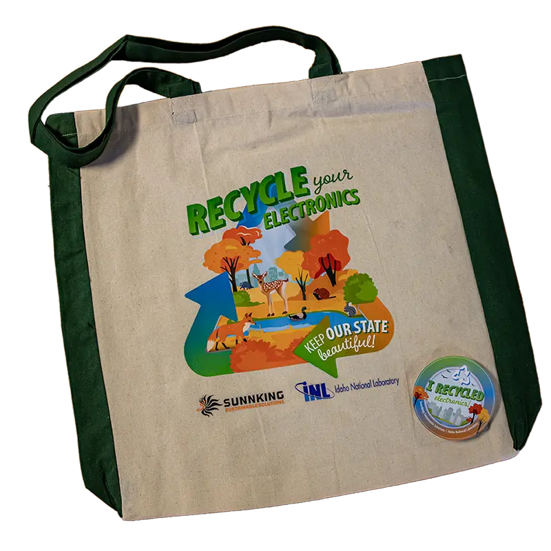 A natural fiber tote bag made with recycled materials featuring a graphic scene of nature in the fall encouraging you to recycle your electronics. Also visible is a circle sticker proudly stating "I Recycled" 