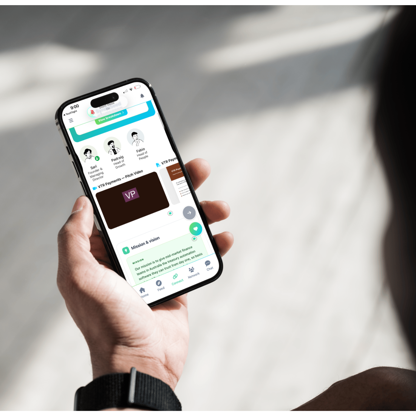 Person outdoors holding a phone showing a SyndeSeed company profile with team members, a pitch video and a mission and vision section.