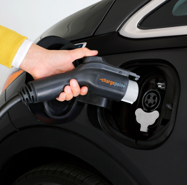 Hand holding ChargePoint plug poised to connect to black electric vehicle charging port.
