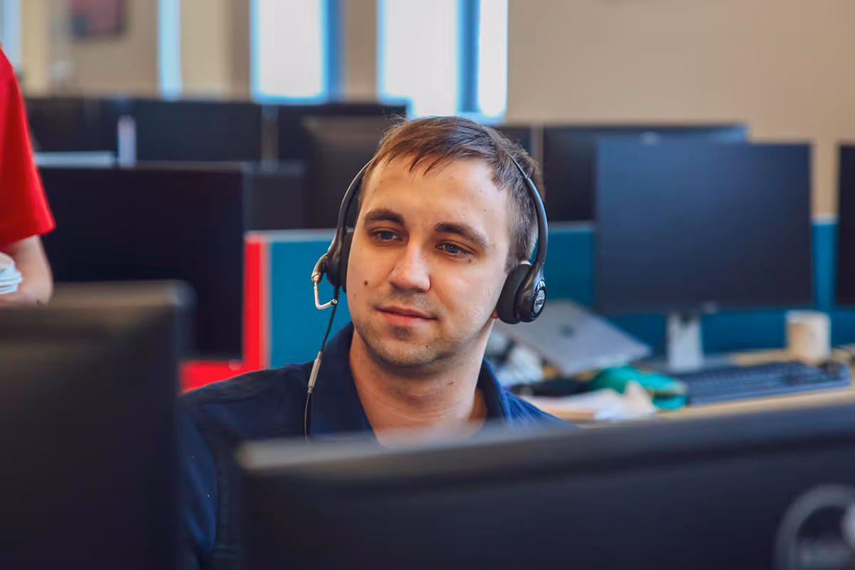 Man wearing headset working on computer in an office with multiple monitors in the background.