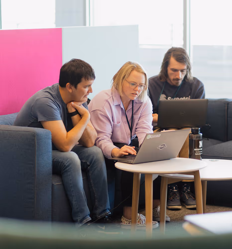 Three people working together on laptops while sitting on sofas in a modern office space.