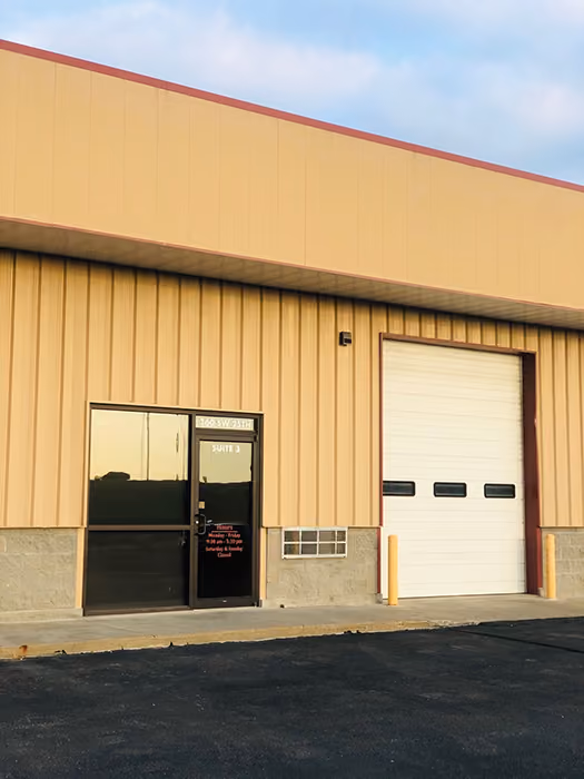 Exterior of a beige industrial building with a glass door and a large white garage door.