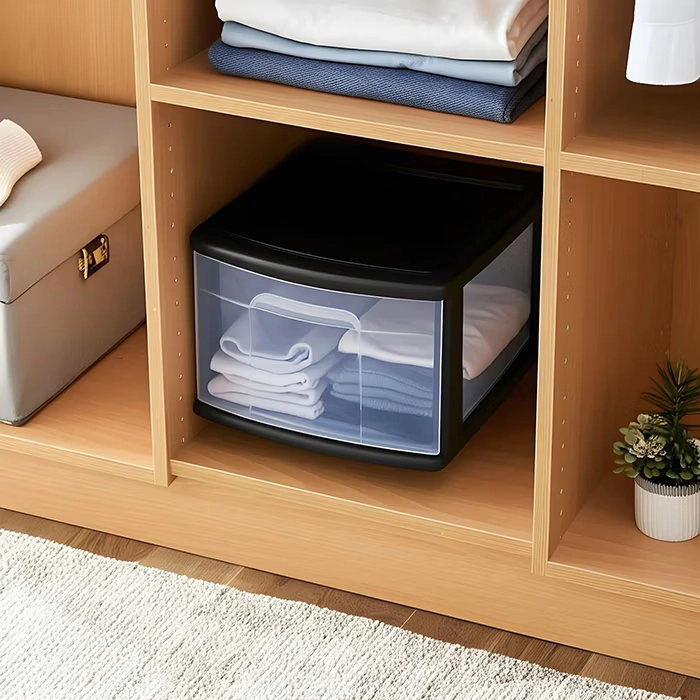 Wooden shelving unit with folded clothes, a black plastic drawer, storage box, and a small potted plant.