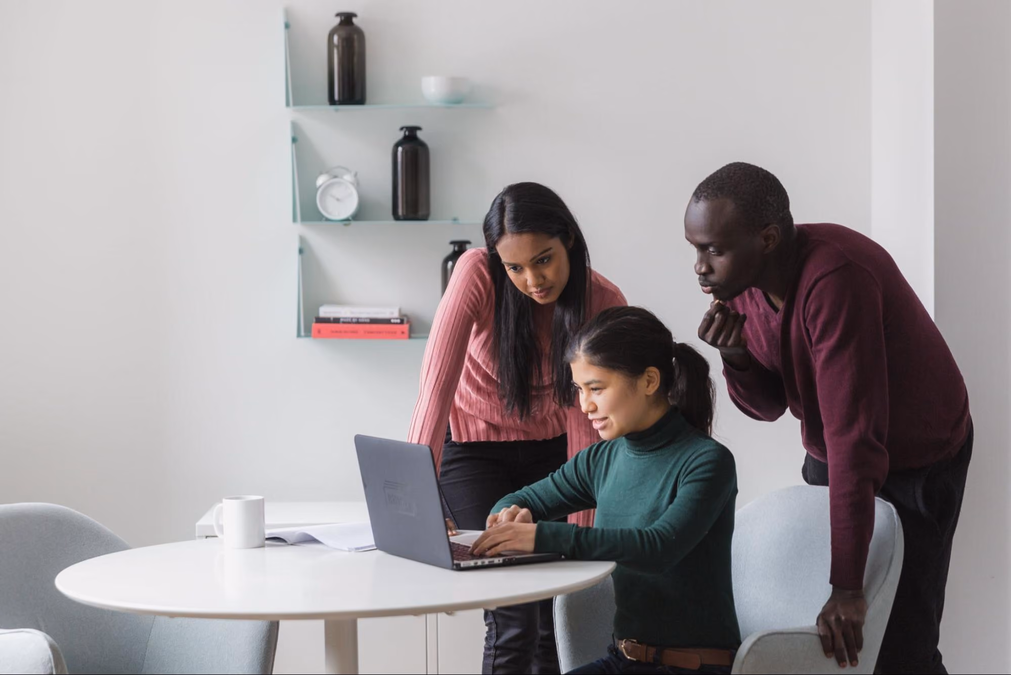 Colleagues peer over an employee’s shoulder to see the laptop screen.