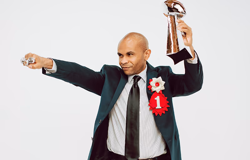 A man wearing a prize rosette and holding a trophy that are employee reward tokens
