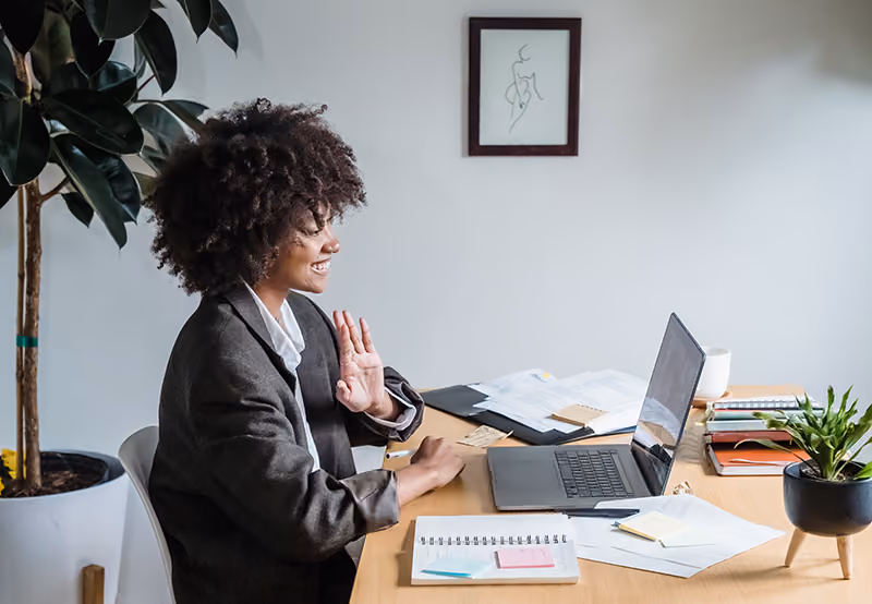 A remote worker greeting colleagues from her home office.