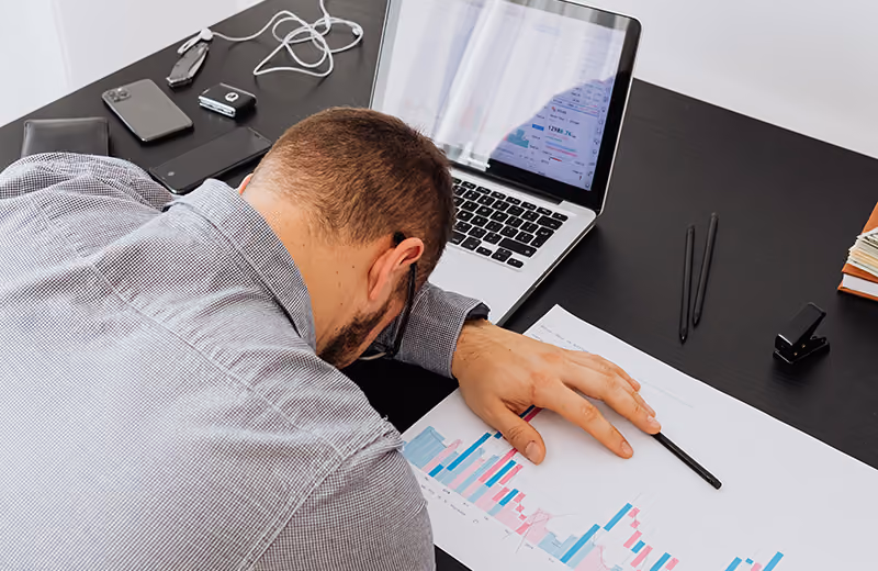 A worker laying their head on their desk because they experience layoff anxiety