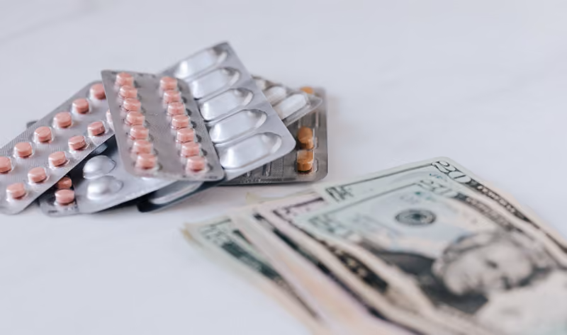Sheets of medication lying next to a stack of 20-dollar bills to depict a healthcare policy that covers employees’ medical expenses.