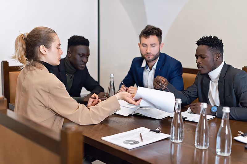 An HR professional explaining insurance benefits to employees in a meeting room and going over the policy’s paperwork with them.