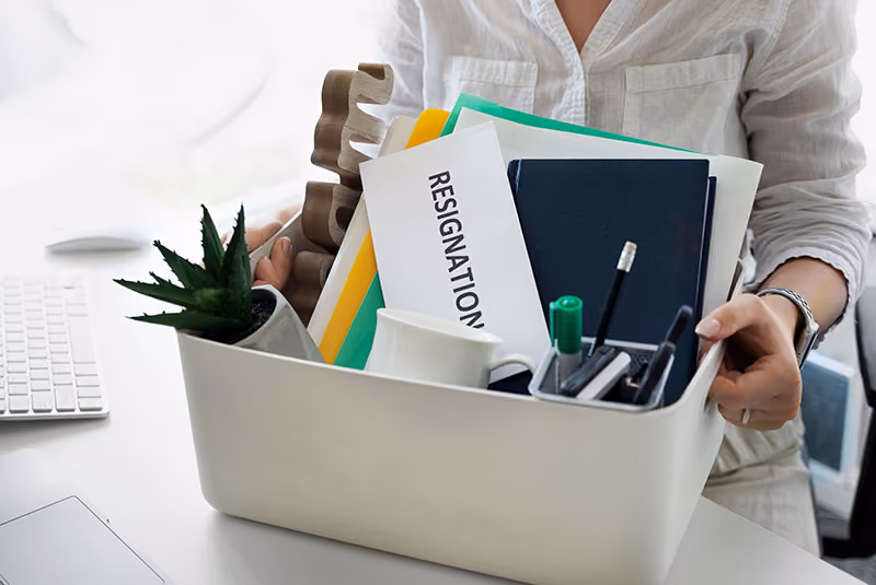 An employee prepares a box of her belongings and a resignation letter to resign from her job.