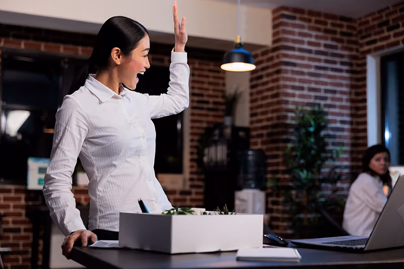 A departing employee greeting her co-workers in a friendly manner as she packs up her desk on her last day of employment