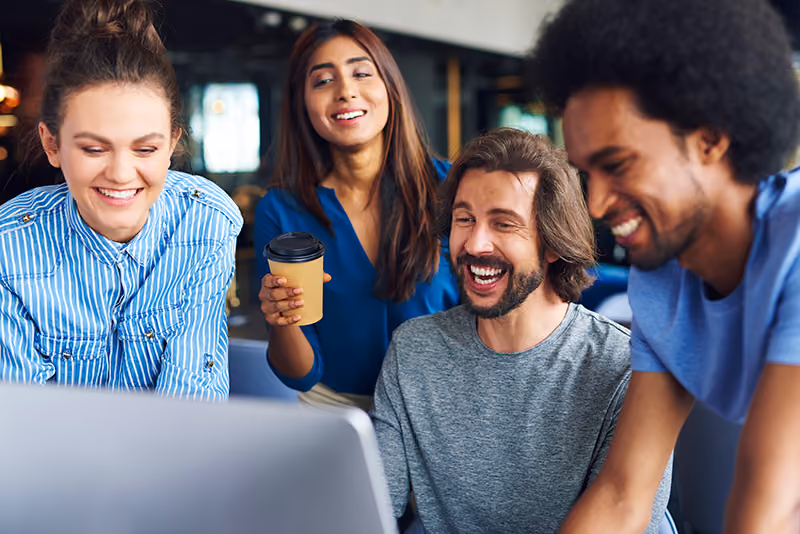 A group of coworkers enjoying a shared moment of laughter at work, indicating their employer has high employee morale.
