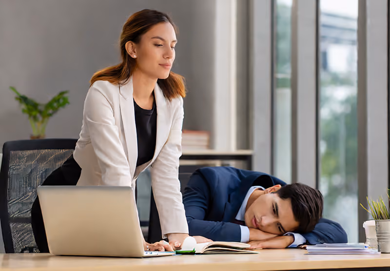 A high-performing employee who is busy next to a lazy employee who is sleeping.