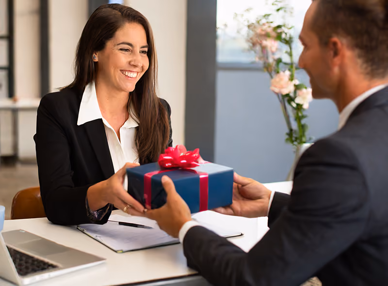 An HR professional receiving a gift from her colleague while sitting at her desk.