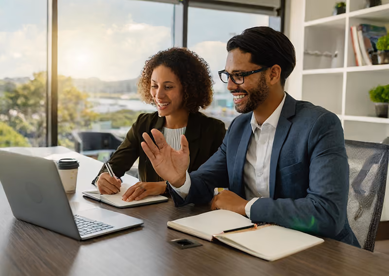 A manager and employee in an office having a video meeting with remote colleagues based elsewhere.