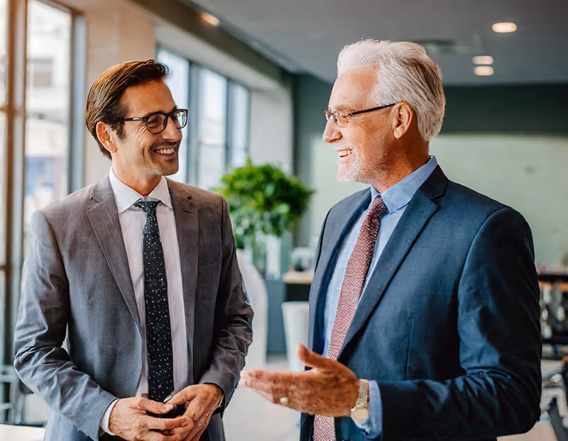 An older professional giving in-person mentorship to a younger employee in an office environment.