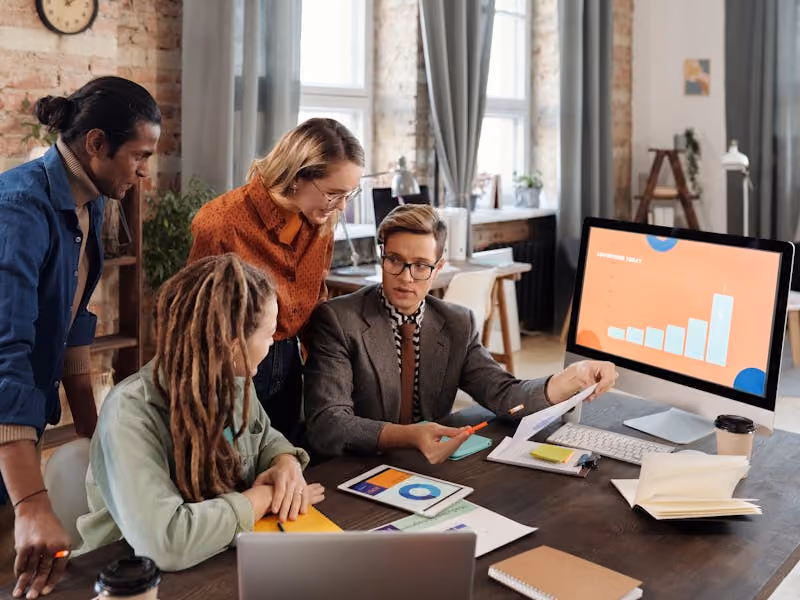 Colleagues gathered around a desk discussing the pros and cons of payroll software and services.