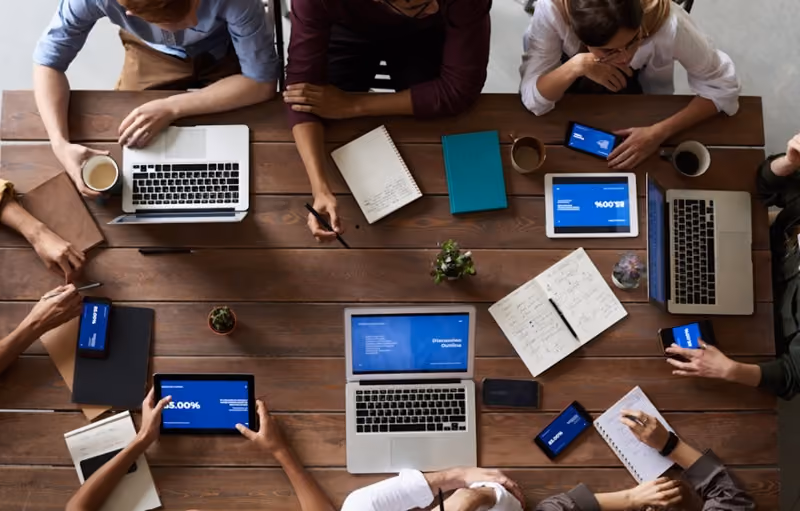overhead view of employees with laptops and notebooks gathered around a desk