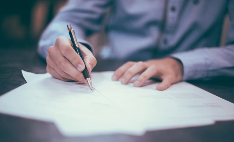 close up of an employee using a pen to edit a series of paper documents.