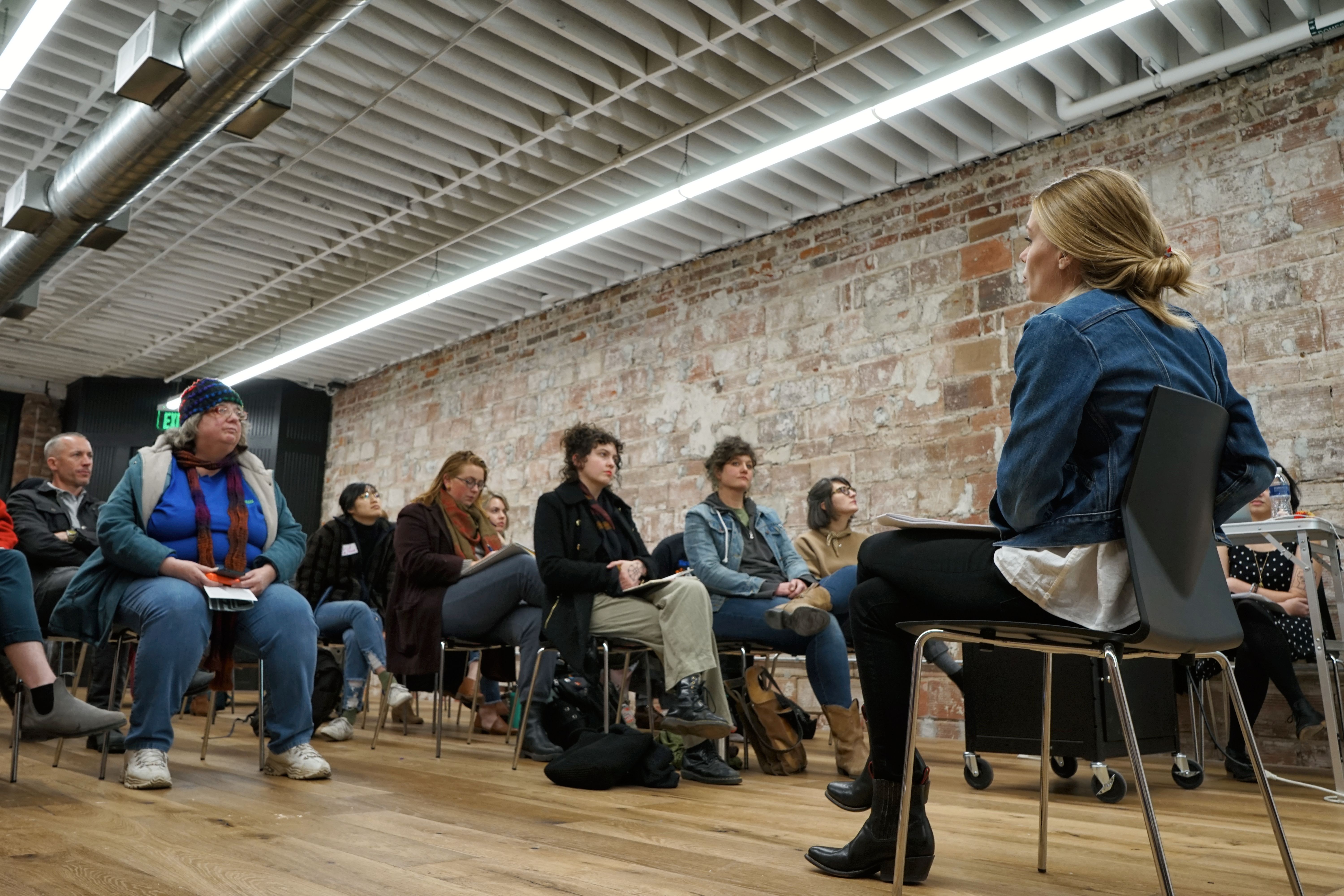 Shelby sits in a black chair and presents to a seated audience.