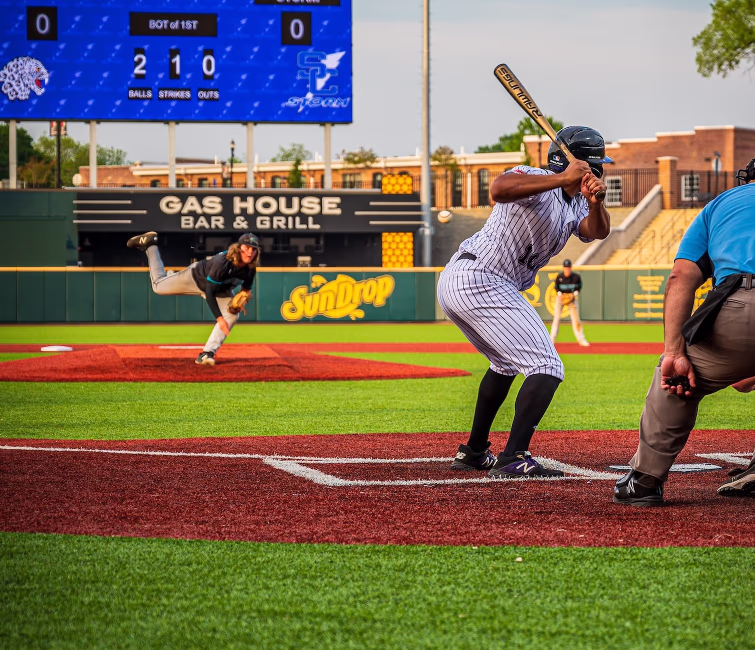 Baseball pitcher in black uniform throwing ball toward batter in striped uniform at home plate.
