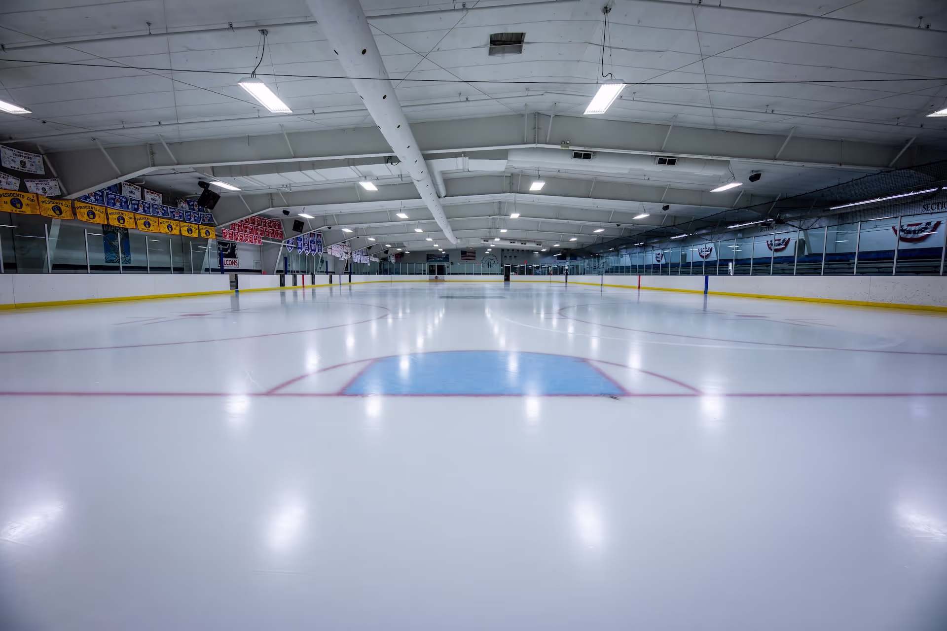 Empty indoor ice hockey rink with banners along the side walls and overhead lighting.