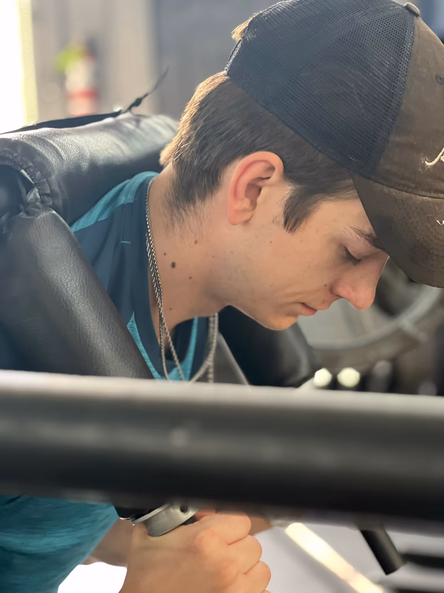 Young man wearing cap and teal shirt working out on gym equipment with focused expression.