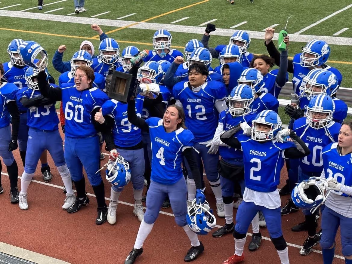 Youth football team in blue Cougars uniforms celebrating a victory holding a trophy and helmets.